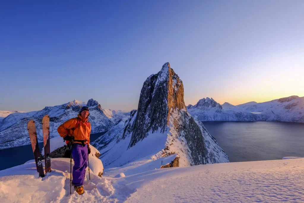 Skitouring man standing at the ridge in front of the iconic Segla mountain, view of the ocean fjords, Fjordgard, Norway